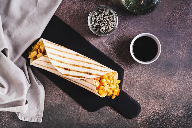 Foto burrito mexicano com frango de milho e pimentas em uma tortilha em uma placa de ardósia vista de cima