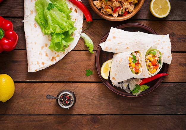 Burritos envolve com carne de frango, milho, tomate e pimentão na mesa de madeira. vista do topo