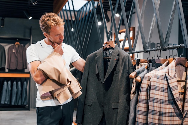 Busca chaqueta Chico joven en una tienda moderna con ropa nueva Ropa elegante y cara para hombres