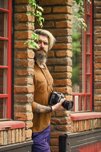 Buscando a alguien brutal hombre viajero con fotografía de cámara retro en la vida moderna consejos de viaje fotógrafo profesional usar cámara hombre barbudo hipster tomar fotos al aire libre