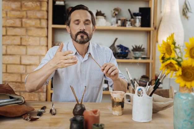 Buscando inspiración. Hombre creativo de pelo oscuro en busca de inspiración mientras quema palos aromáticos en su taller