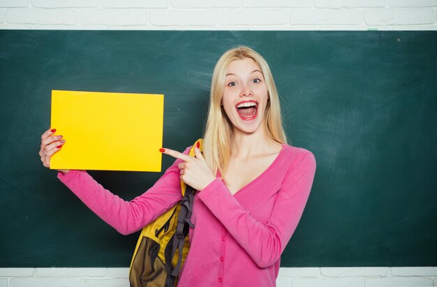 Buscando voluntarios Educación secundaria Educación formal Mejorarme a través de la educación Niña feliz sosteniendo un libro y mirando a la cámara mientras está de pie en el aula Estudiante con mochila