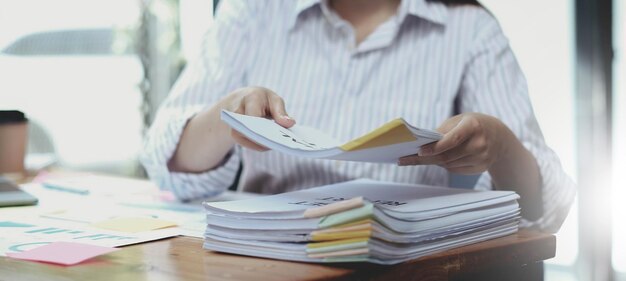 Business Documents Konzept Mitarbeiterin Hände arbeiten in Stacks Papierakten zum Suchen und Überprüfen von unfertigen Dokumenten erreicht auf Ordnerpapieren im geschäftigen Büro Weicher Fokus