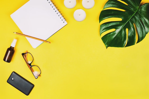 Business Flatlay mit Handy, Brille, Philodendronblatt und anderem Zubehör. Gelber Hintergrund.