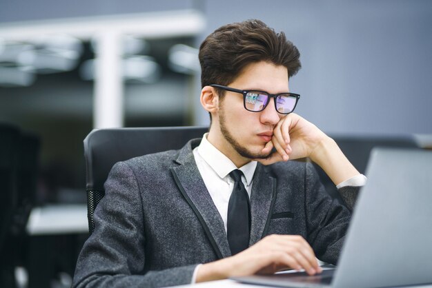 Business-Manager mit Brille arbeitet an seinem Laptop im Büro. Junger Freiberufler, der von einem Laptop aus arbeitet.