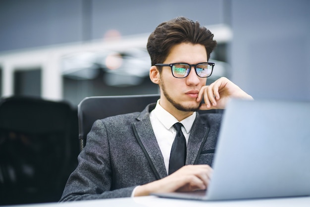 Business-Manager mit Brille arbeitet an seinem Laptop im Büro. Junger Freiberufler, der von einem Laptop aus arbeitet.