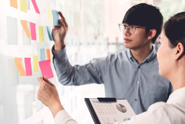 Business Manager zeigt Idee für ihr Team und kleben viele Memopapier auf Glasfenster an die Arbeit