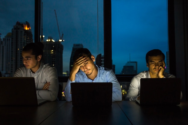Business-Team arbeitet spät in der Nacht mit Licht aus und Computer Laptop-Bildschirm Licht an