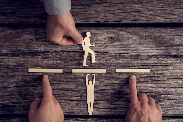 Business-Teamwork-Konzept mit den Händen von drei Geschäftsleuten, die Papierausschnitte von zwei Männern über rustikalem Holz mit Kopierraum unterstützen oder unterstützen.
