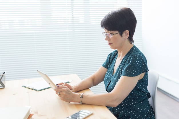 Business-, Technologie- und Personenkonzept - eine ernsthafte Frau, die im Büro sitzt und ein Tablet verwendet