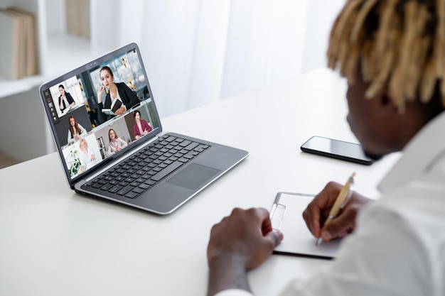 Business-Webinar Video-Chat Fernunterricht Typ, der Online-Unterricht mit weiblichen Trainern ansieht, die Studenten sprechen, die sich Notizen auf dem Laptop-Bildschirm in der virtuellen Klasse machen