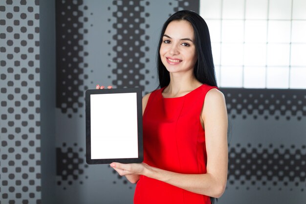 Businesslady atractiva en vestido rojo muestra tableta vacía