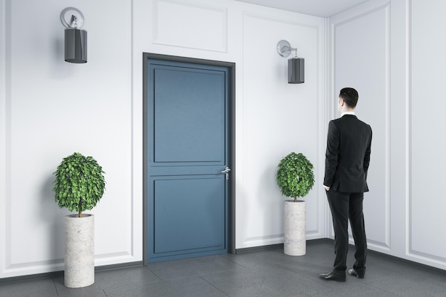 Businessman standing in empty room with blue door and two plants