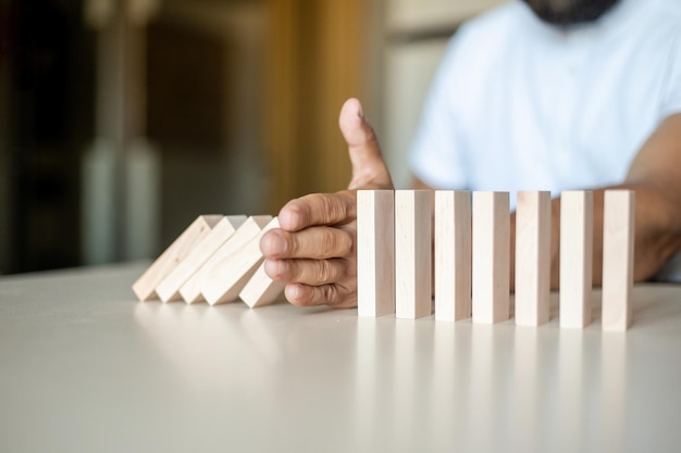 Foto businesswoman stoppt holzblock, der in der domino-linie fällt, mit investitionsversicherung alternative und verhinderung geschäftsrisiko-conto-konzept