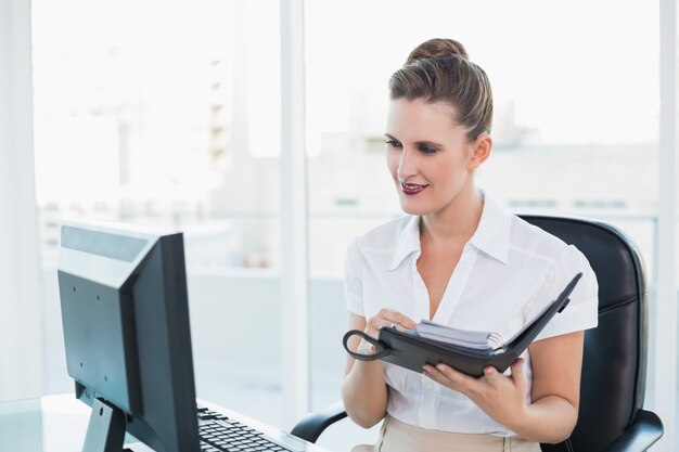 Businsswoman mirando la pantalla de la computadora mientras sostiene la agenda