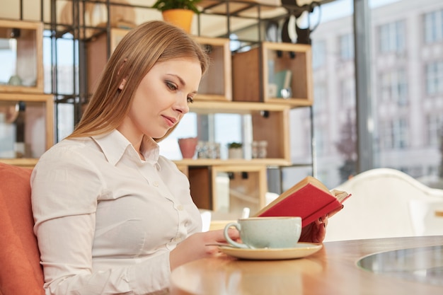 Busnesswoman novo encantador que lê um livro, relaxando na cafetaria