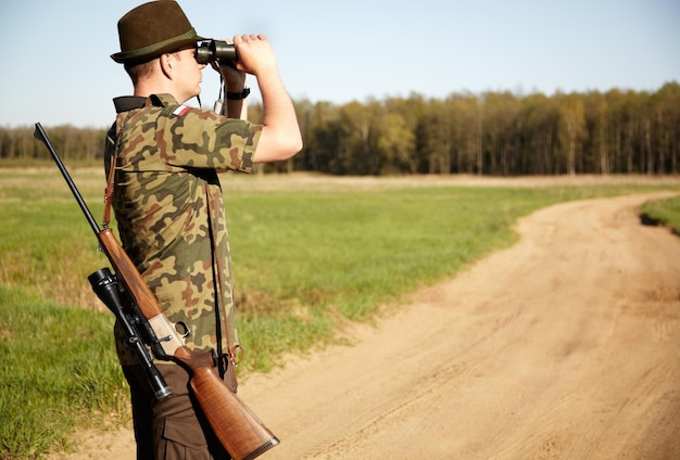 En la búsqueda Un guardabosques con su rifle mirando a través de sus binoculares al aire libre con copyspace