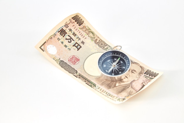 Bússola com notas de iene japonês e moeda de iene japonês em fundo branco