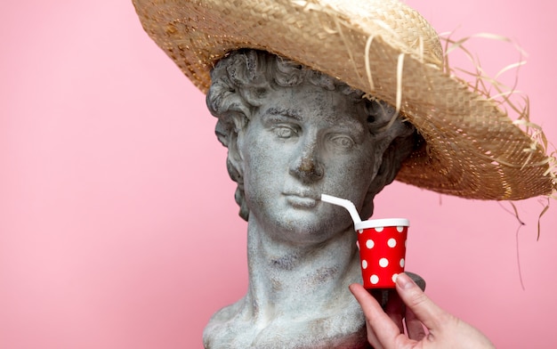 Busto antiguo del varón en sombrero con la bebida de la cola en fondo rosado.