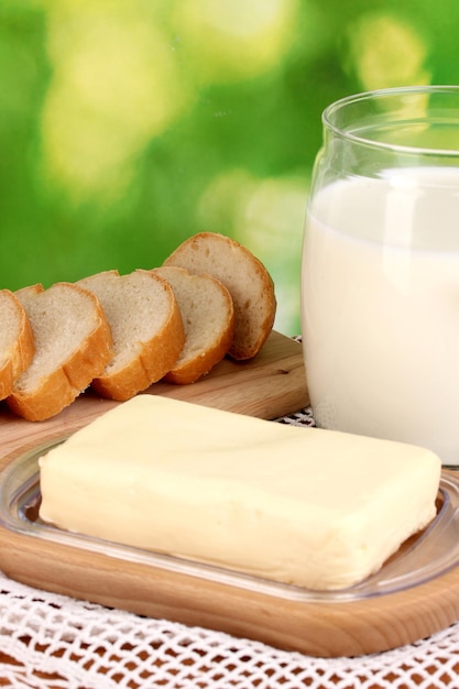 Butter auf Holzhalter, umgeben von Brot und Milch auf natürlichem Hintergrund, Nahaufnahme