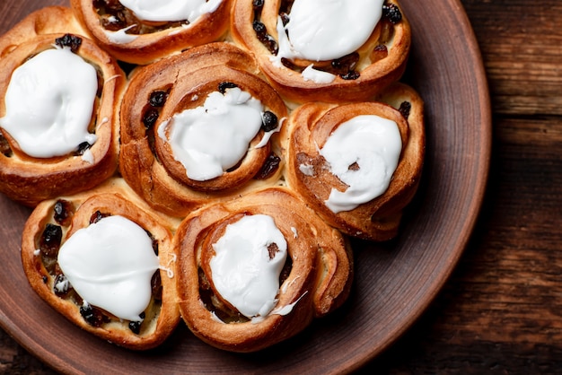 Buttersüße Brötchen mit Rosinen auf einer braunen Tonplatte. Mit Weißzuckersirup bedeckt.