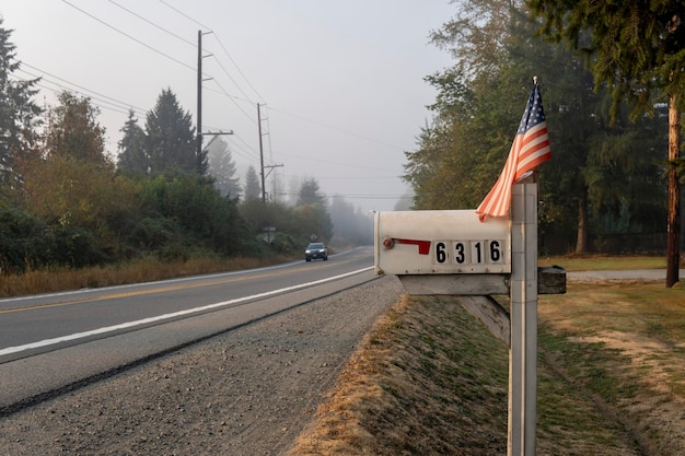 Buzón de correo americano típico al aire libre con bandera americana en el lado de la carretera