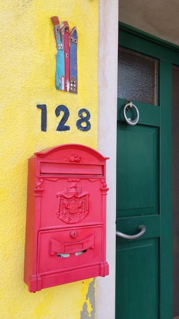 Foto buzón rosa en una pared amarilla, junto a una puerta verde, en la isla de burano, italia.