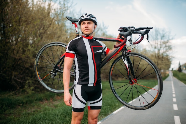 Bycyclist mantiene la bicicleta sobre el hombro después de andar en bicicleta