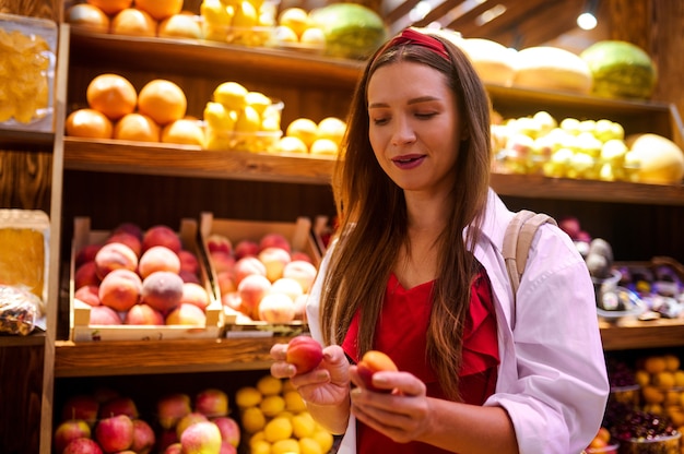 Bying frutas. Una linda mujer con una naranja en la mano de pie en una tienda de frutas