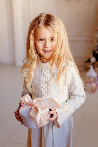 C Menina loira bonita com vestido perto da árvore de Natal