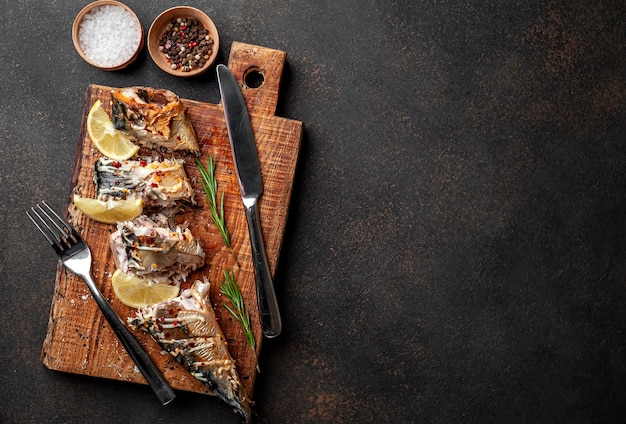 caballa al horno sobre una tabla para cortar con limón y especias sobre un fondo de piedra