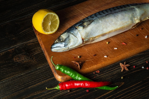 Caballa cruda o pescado Scomber en la tabla de cortar de la cocina antes de cocinar con especias, pimienta y limón