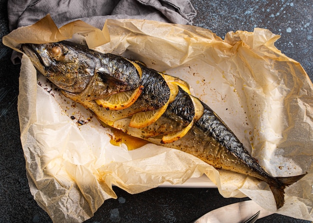 Caballa entera o pescado scomber con limón y hierbas al horno y servido en papel de horno desde arriba. Delicioso pescado sano asado en la vista superior de fondo de hormigón