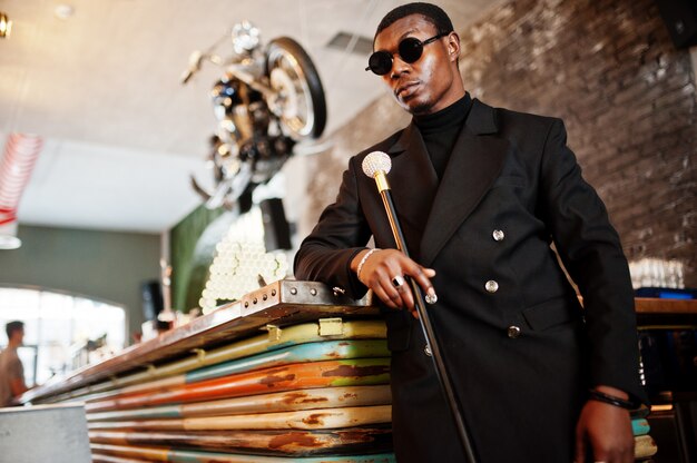 Caballero elegante con elegante chaqueta negra y gafas de sol, con bastón retro como matraz de caña