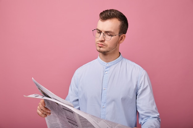 Caballero inteligente con una camisa azul claro con gafas y un periódico en las manos.