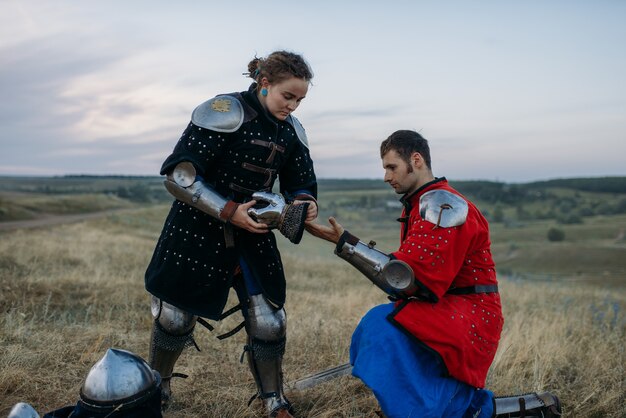 El caballero medieval ayuda a su amigo a ponerse la armadura, gran torneo. Antiguo guerrero blindado con armadura posando en el campo