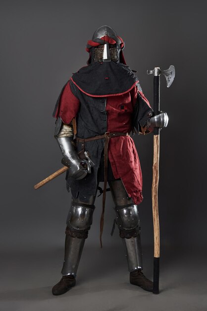 Foto caballero medieval sobre fondo gris retrato de un brutal guerrero de cara sucia con armadura de malla roja y negra ropa y hacha de batalla