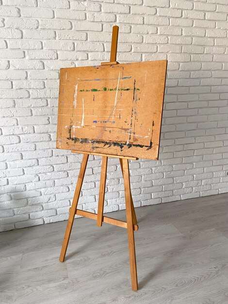 Un caballete de artistas se encuentra elegantemente contra una pared de ladrillo blanco texturizado con lienzo de madera bien utilizado