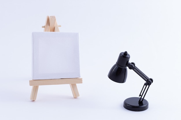 Caballete en miniatura de madera con lienzo cuadrado blanco en blanco y lámpara de mesa