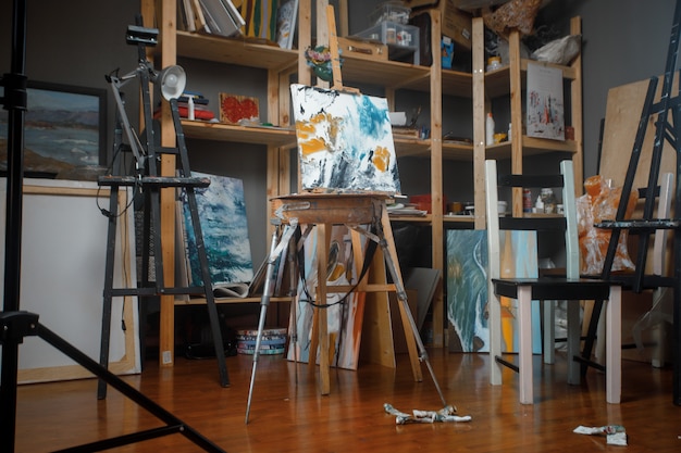Caballete, pinceles, pinturas y paleta en un taller de arte.