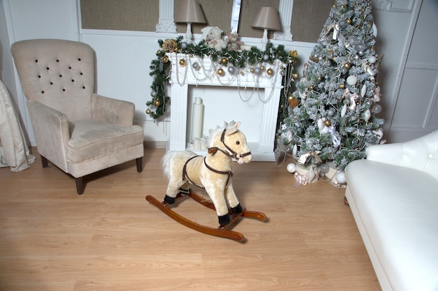 Un caballo de juguete se encuentra cerca de un árbol de Navidad decorado y brillante y un sillón.