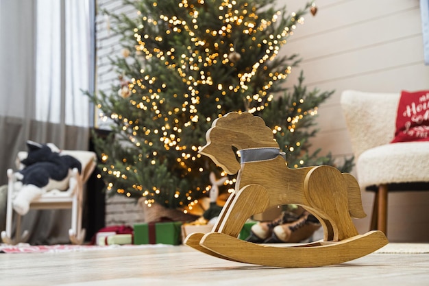 Caballo de juguete mecedora en el suelo en el salón interior con árbol de Navidad en segundo plano.