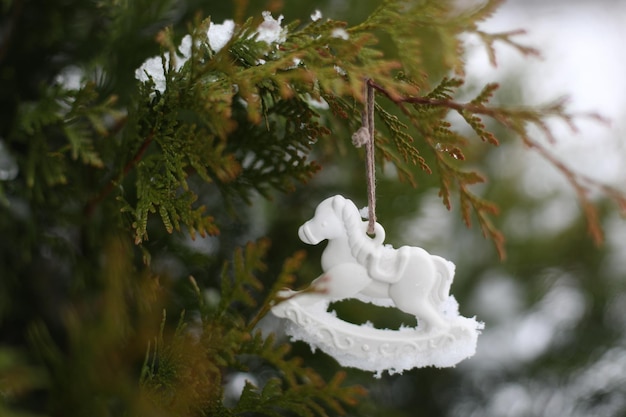 Caballo de juguete de Navidad colgando de ramas verdes en la nieve en invierno Árbol de Navidad Caballo de juguete Regalo Decoración de Año Nuevo