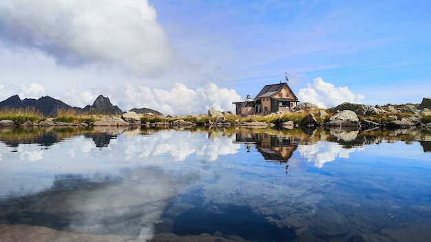 Cabana alpina é refletida em um pequeno lago na montanha