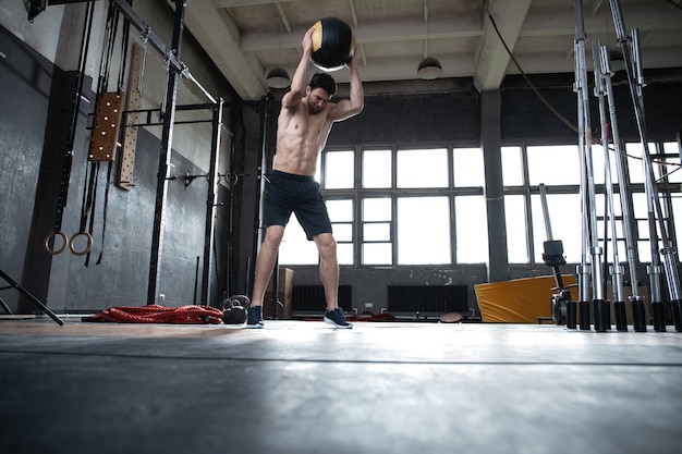 Cabe o homem jogando medicine ball fazendo ball slam contra o chão do ginásio ou exercícios de treino da parte superior do corpo de imprensa de ombro. Treinamento cruzado no centro de fitness.