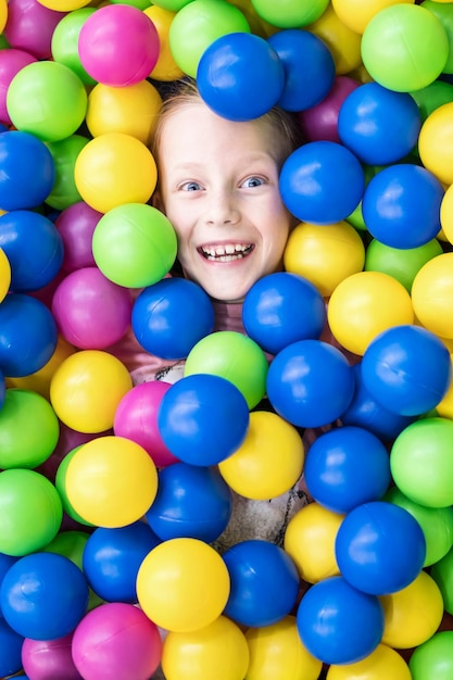 Cabeça de uma criança rindo espreita de uma pilha de bolas coloridas