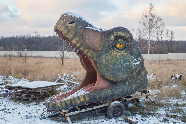 Cabeça enorme abandonada de dinossauro decorativo no gramado de inverno