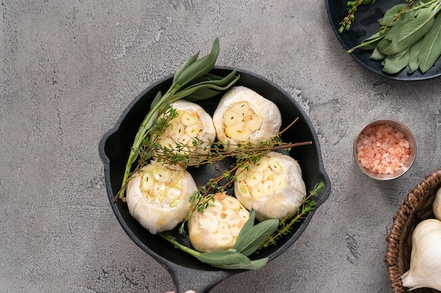 Cabeças de alho cru com especiarias frescas em frigideira de ferro fundido para preparar receita de alho assado.