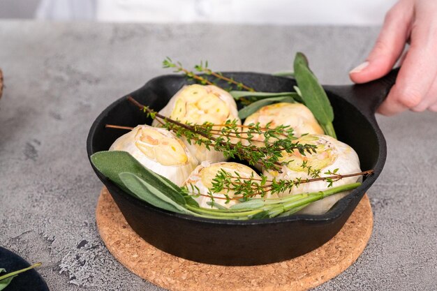 Cabeças de alho cru com especiarias frescas em frigideira de ferro fundido para preparar receita de alho assado.