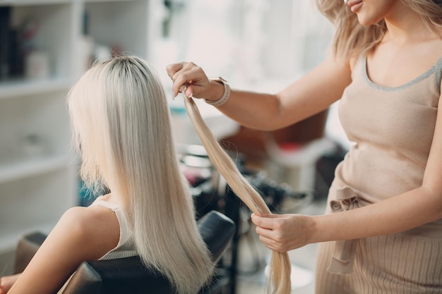 Cabeleireira fazendo extensões de cabelo para jovem loira em extensão de cabelo profissional de salão de beleza